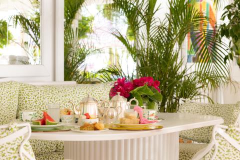 This image features a beautifully arranged table set for tea in a bright, plant-filled room