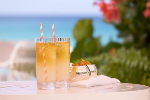 The image features two glasses of a yellowish, iced drink, possibly a lemonade or cocktail, served with straws that have a red and white spiral design