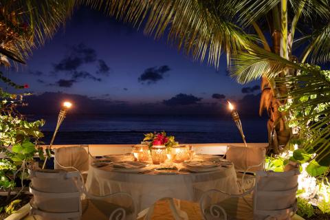 This image shows a romantic dining setup by the beach at dusk