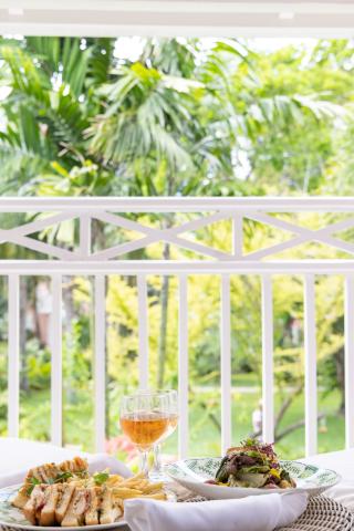 The image features a dining setup on a balcony overlooking a garden with lush greenery
