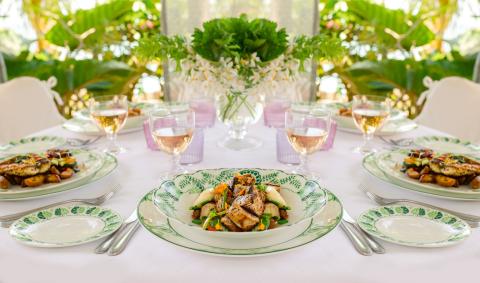The image shows an elegant dining setup, possibly at an outdoor location given the greenery in the background