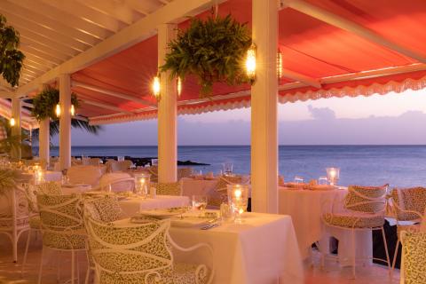 This image captures a beautifully set seaside outdoor dining area during what appears to be twilight