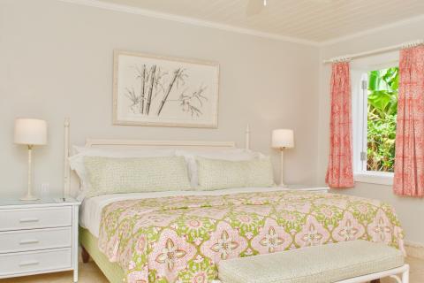 The image shows a bedroom with a neatly made bed featuring a green and pink patterned comforter and multiple pillows