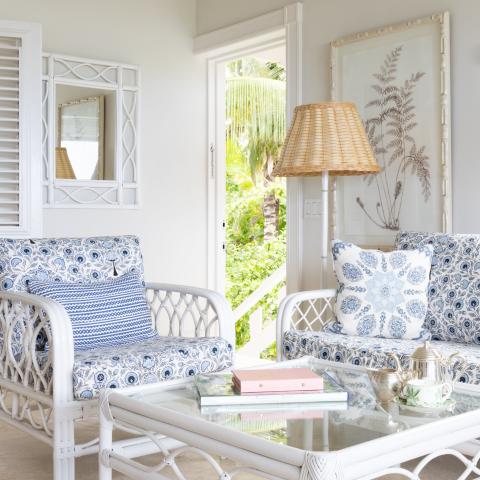 The image features a stylish indoor sunroom area furnished with bamboo-style white furniture that has blue and white patterned cushions