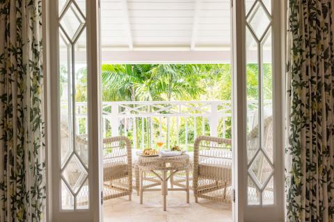 The image shows a view through an open doorway leading to a balcony in a tropical setting