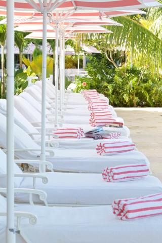 This image shows a line of white sun loungers covered with white towels, each adorned with a rolled-up red and white striped towel