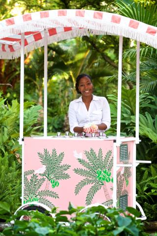 This image features a smiling woman operating a charming, pink cart under a striped umbrella