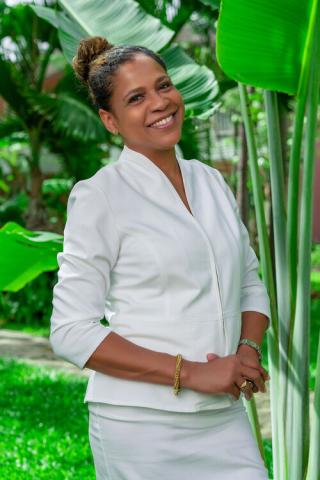 The image features a woman wearing a white blazer standing in a lush, green garden