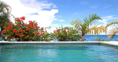 The image shows a beautiful tropical scene with an outdoor swimming pool in the foreground