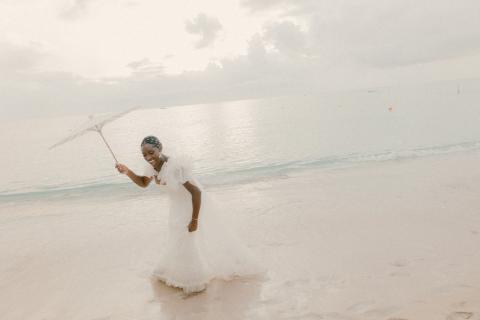 The image shows a joyful woman dressed in a white wedding gown, frolicking on a sandy beach
