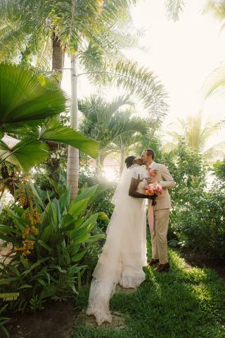 This image captures a romantic moment between a bride and groom in a lush, tropical setting