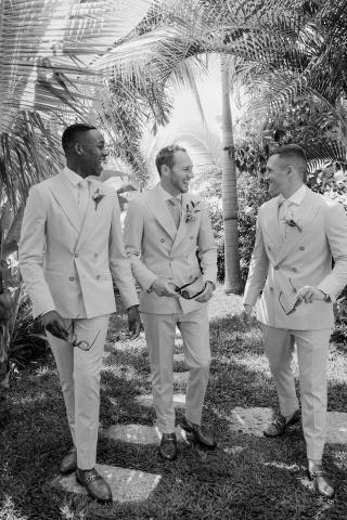 This image features three men dressed in elegant light beige double-breasted suits, possibly at a wedding or formal event, given the matching attire and boutonnieres