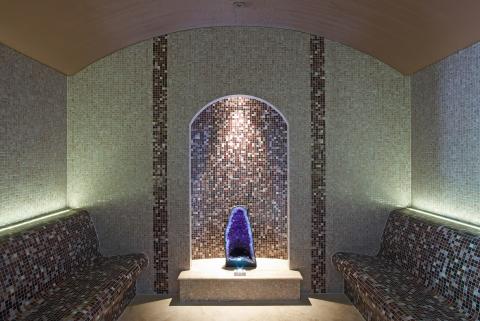 The image shows an interior space featuring an alcove or niche with an arched ceiling and walls decorated in small mosaic tiles, predominantly in shades of beige with some accents in dark brown