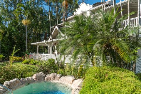 This image showcases a lush, tropical setting with a traditional white house featuring verandas and colonial-inspired architecture