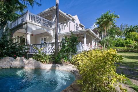 The image features a charming, luxurious two-story house with architectural influences that suggest a tropical or Caribbean style