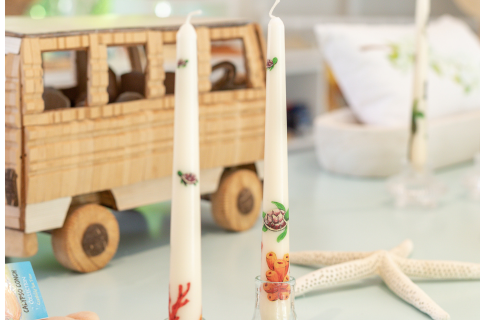 This image features a detailed wooden model of a bus positioned on a table, next to two decorated candles