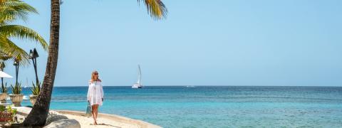 This image features a coastal scene with a woman standing on a sandy beach under a sunny sky