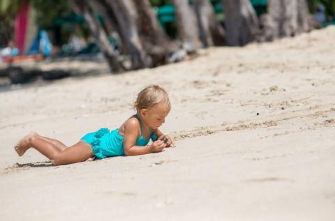 The image shows a young child lying on a sandy beach
