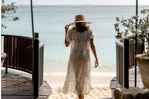 This image shows a woman standing on a wooden boardwalk leading to a beach