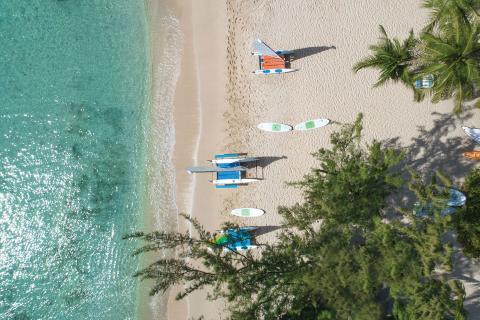 This image shows a beautiful overhead view of a sandy beach meeting clear turquoise waters