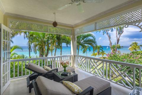 This image showcases an idyllic tropical beachfront view seen from an open, covered patio