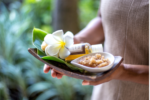 This image depicts a person holding a tray with various spa products and a fresh flower