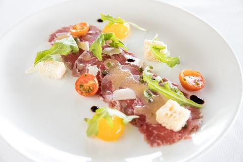This image displays an elegantly presented dish that appears to be carpaccio, which is thinly sliced raw meat, likely beef, garnished with various ingredients