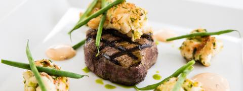 This image features a gourmet dish consisting of a grilled steak topped with what appears to be sautéed shrimp or lobster