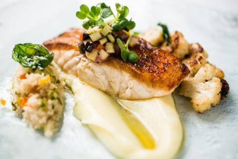 This image features a gourmet dish consisting of seared fish fillet topped with a colorful diced vegetable relish and microgreens