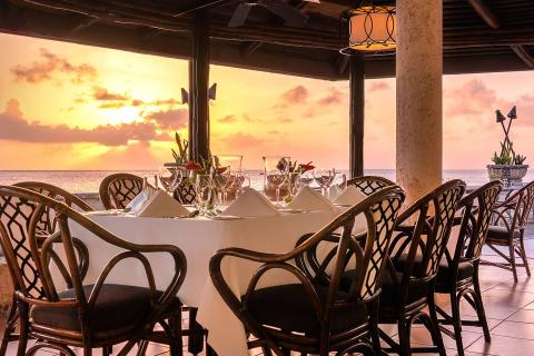 This image features a beautifully set dining area in a seaside restaurant during sunset