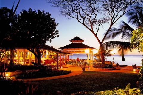 This image shows a beautifully lit outdoor dining area during evening time, by the seaside