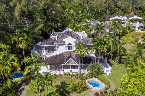 This image features a luxurious tropical estate with a series of buildings surrounded by lush greenery and palm trees
