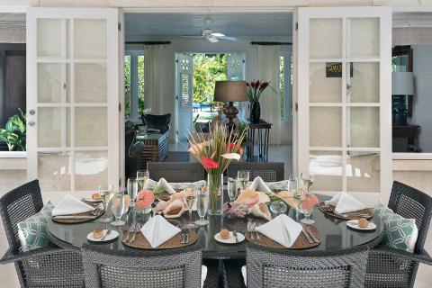 This image shows a beautifully arranged dining area set on a patio, likely part of a tropical or subtropical resort or home