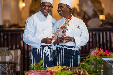 The image depicts two chefs, a man and a woman, in a restaurant or a buffet setting