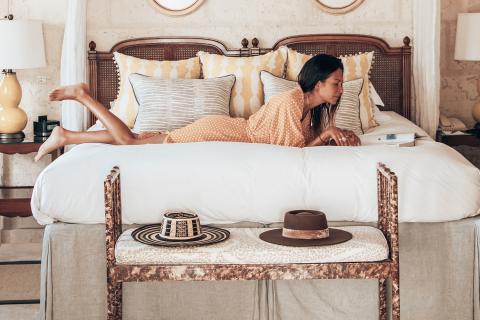 The image shows a woman relaxing on a bed in a room that has a vintage or rustic decor style