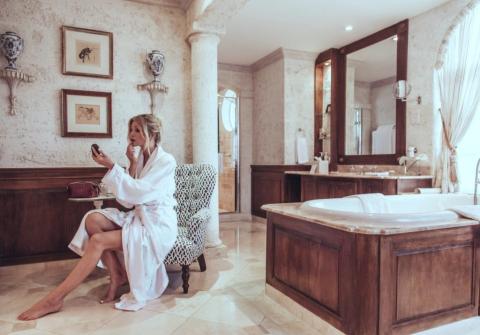 The image shows a woman sitting on a chair in a luxurious bathroom