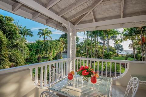 The image shows a well-furnished porch or balcony of a house with a tropical view