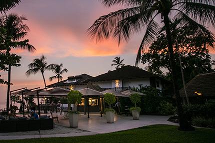 The image features a tropical outdoor setting at dusk with a picturesque sunset in the background