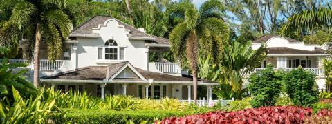 The image features a tropical setting with a beautifully manicured landscape dominated by a variety of lush greenery and vibrant red plants in the foreground