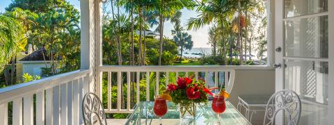 The image displays a picturesque view from a balcony overlooking a lush, tropical landscape