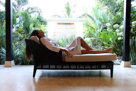 The image shows a woman reclining comfortably on a wicker lounge chair