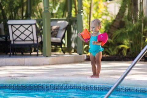 In the image, there is a young child standing next to a swimming pool