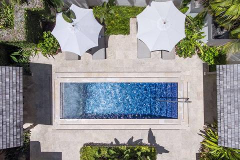 This image shows an overhead view of an outdoor area featuring a long, narrow swimming pool surrounded by a landscaped terrace