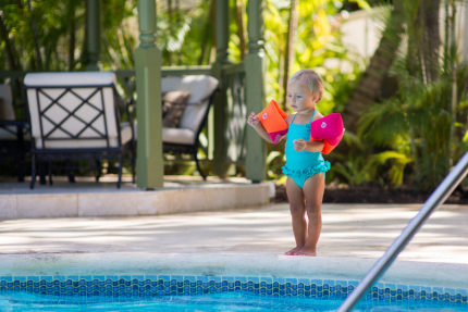 The image shows a young child standing by the edge of a swimming pool