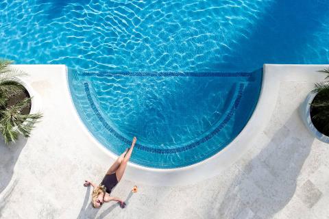 This image shows a woman lying down beside a luxurious swimming pool
