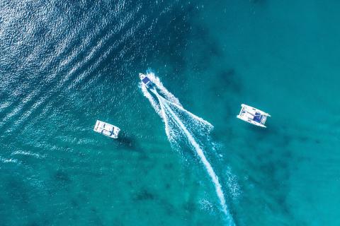The image shows an aerial view of three boats on a body of clear blue water
