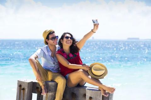 This image features a couple sitting on a wooden dock, taking a selfie with a smartphone