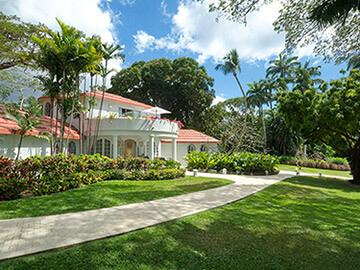 The image shows a large, elegant house surrounded by lush, green landscaping