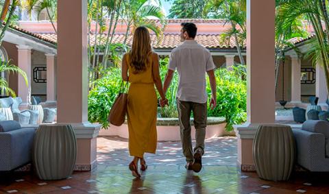 This image encapsulates a scenic and serene moment featuring a couple walking through a beautifully designed corridor framed by archways and columns