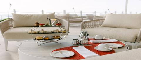 This image features an elegant outdoor dining setting, likely at a beachside or coastal location, given the presence of a sandy environment and sea visible in the background